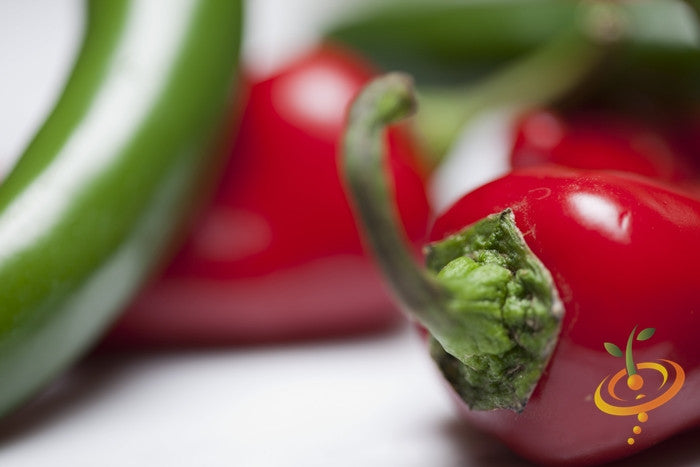 Thai hot pepper seeds from SeedsNow, showing vibrant green pepper seeds with some mature red peppers in the background.